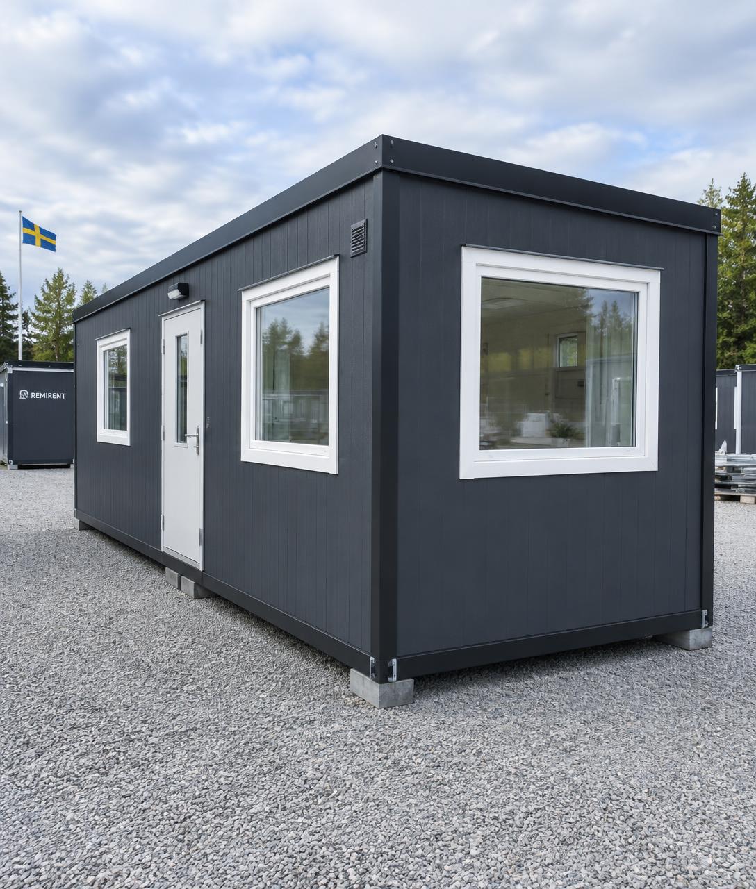 Nyrenoverad mörkgrå modulbod på grusplan